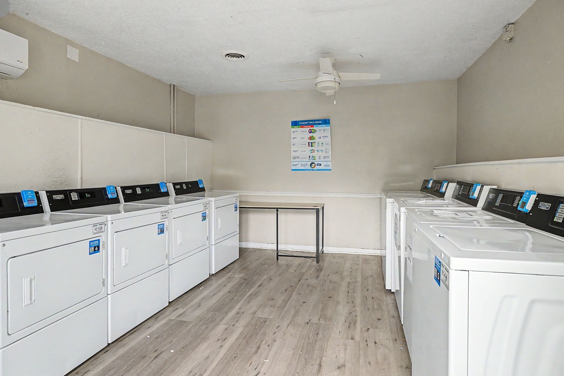 Laundry room with rows of white washers and dryers, a folding table, and a wall sign.