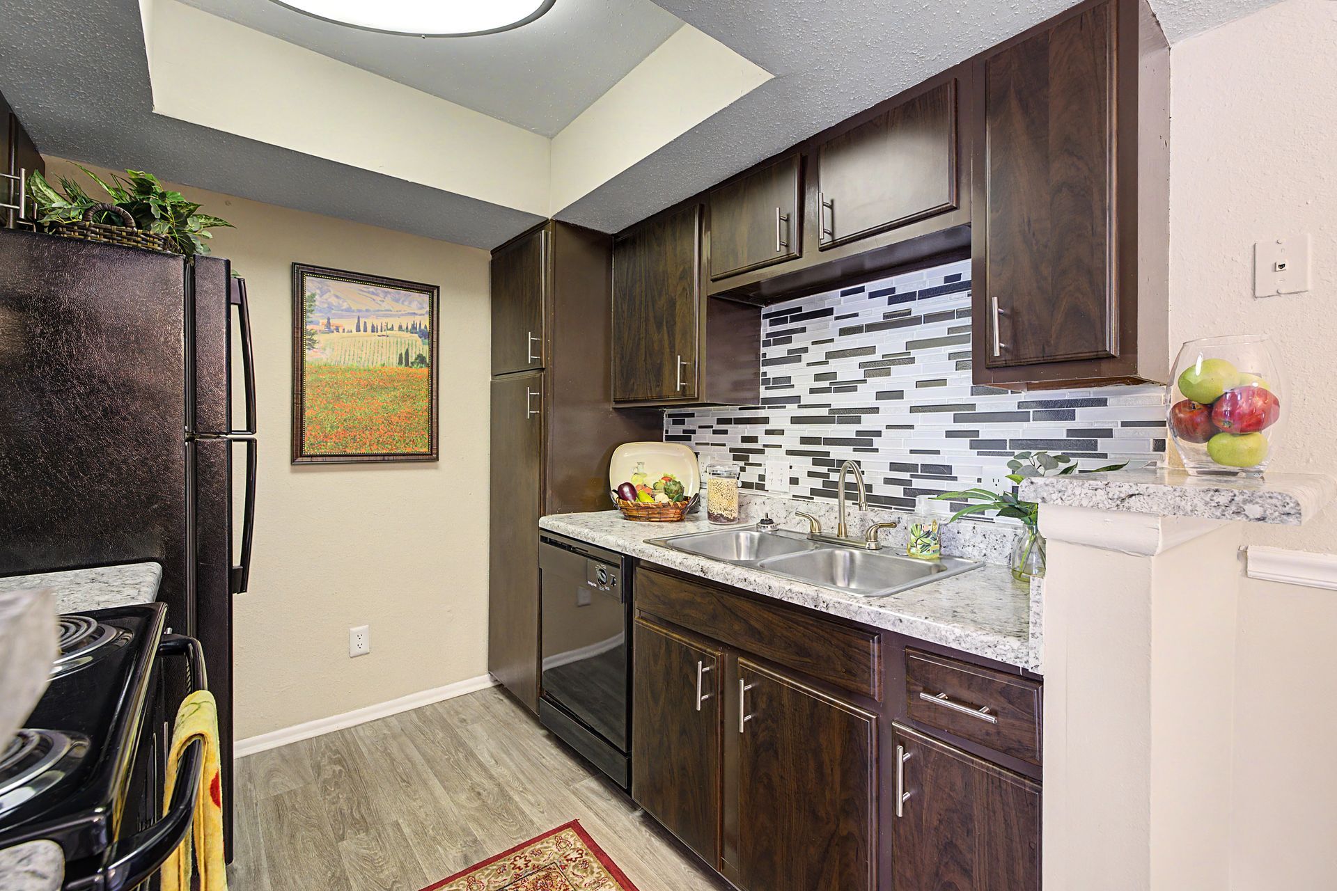 Compact kitchen with dark wood cabinets, granite counter, mosaic backsplash, and refrigerator on the left.