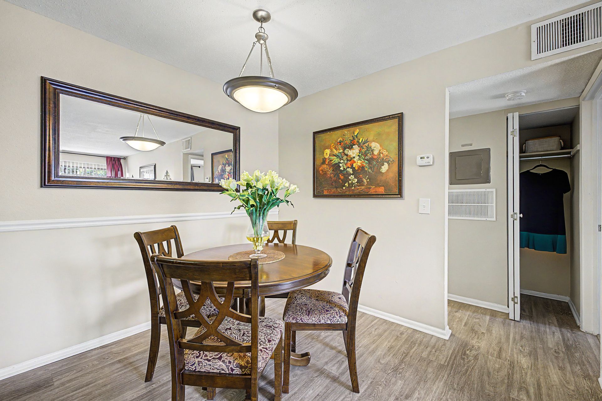 Dining room with round table, wooden chairs, large mirror, and wall art in a bright neutral interior.
