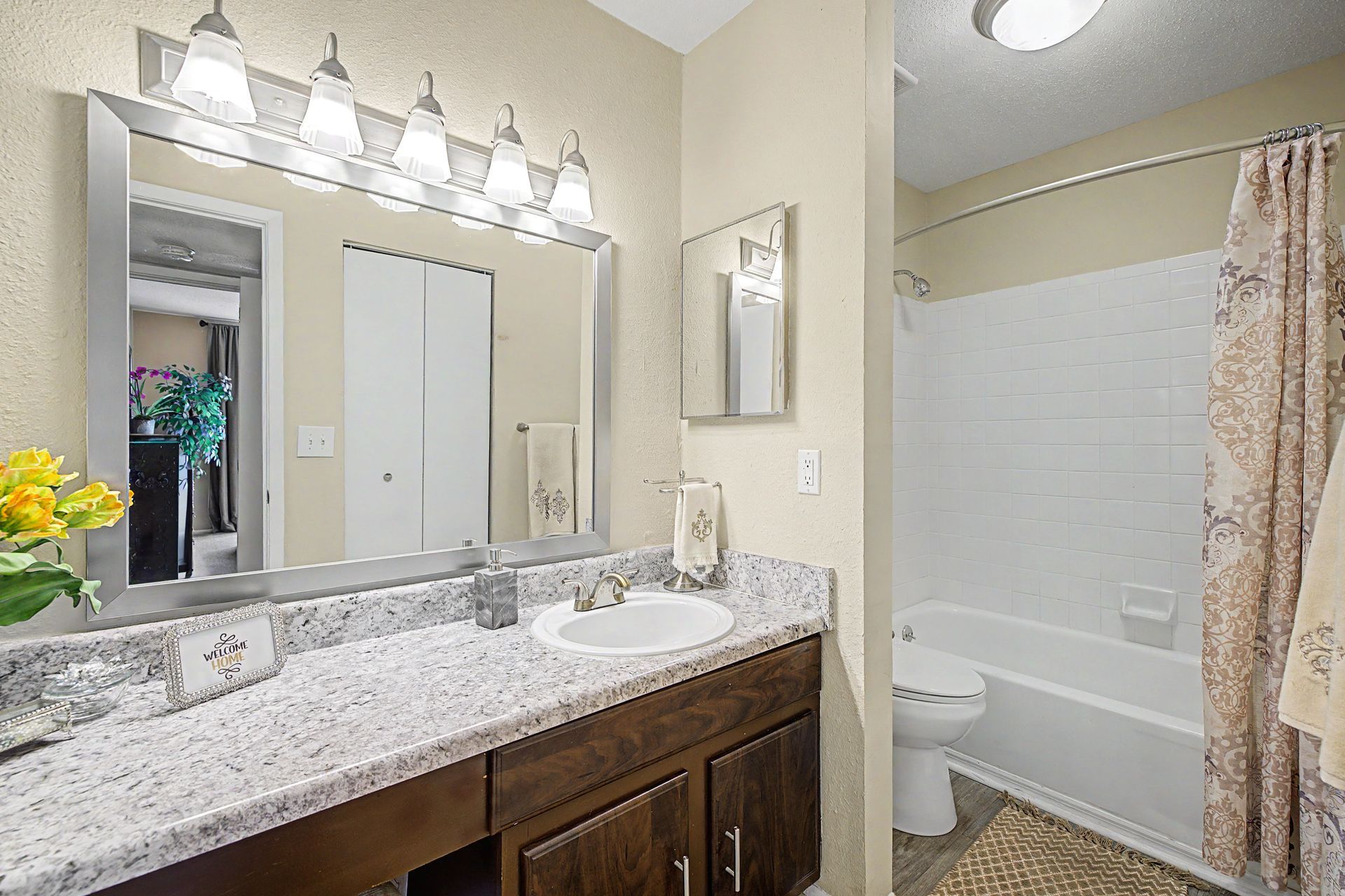 Bright bathroom with granite vanity, large mirror, lights, and a shower with white curtain and tiled walls