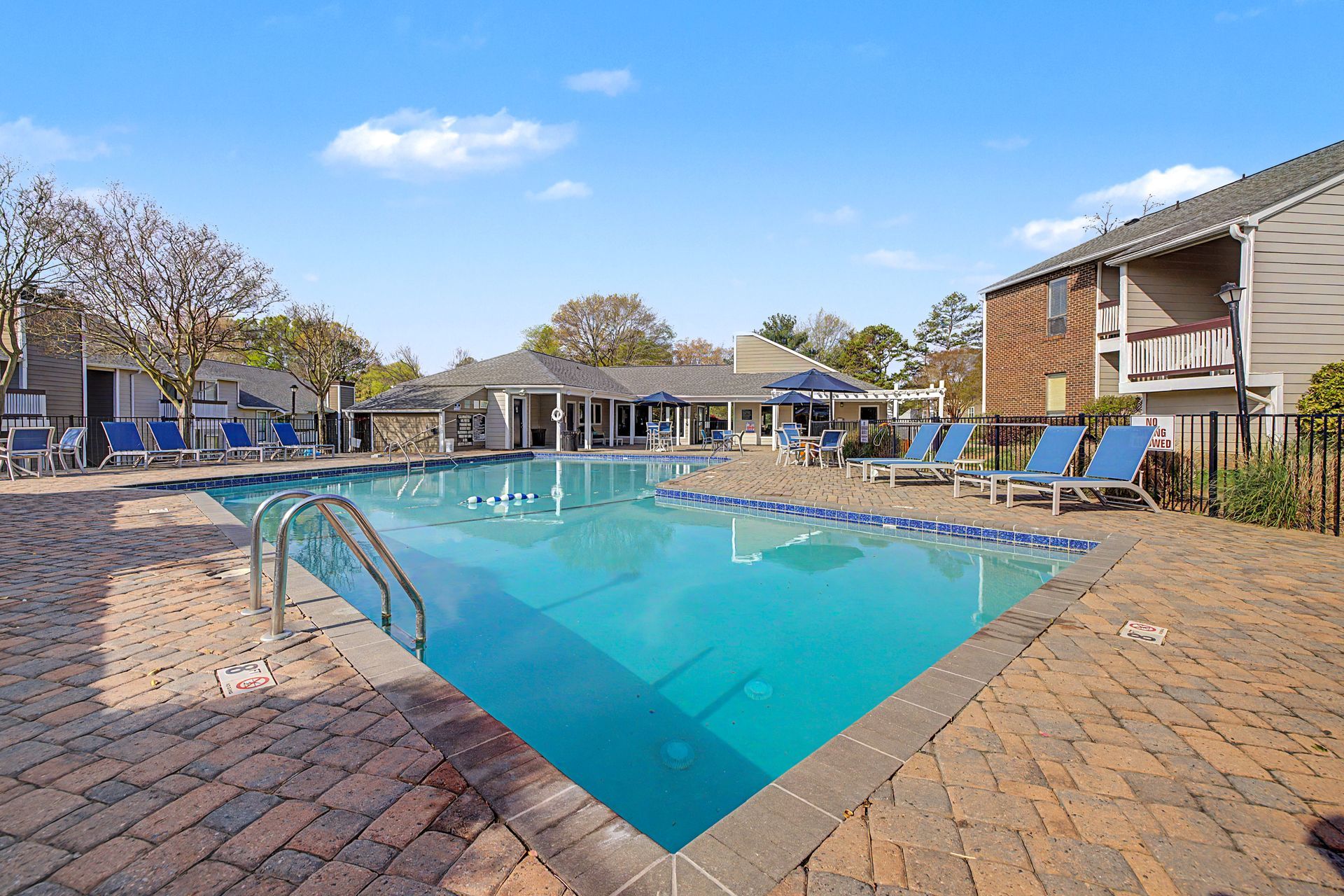 Outdoor apartment pool with blue water, lounge chairs, and brick deck under a clear sky