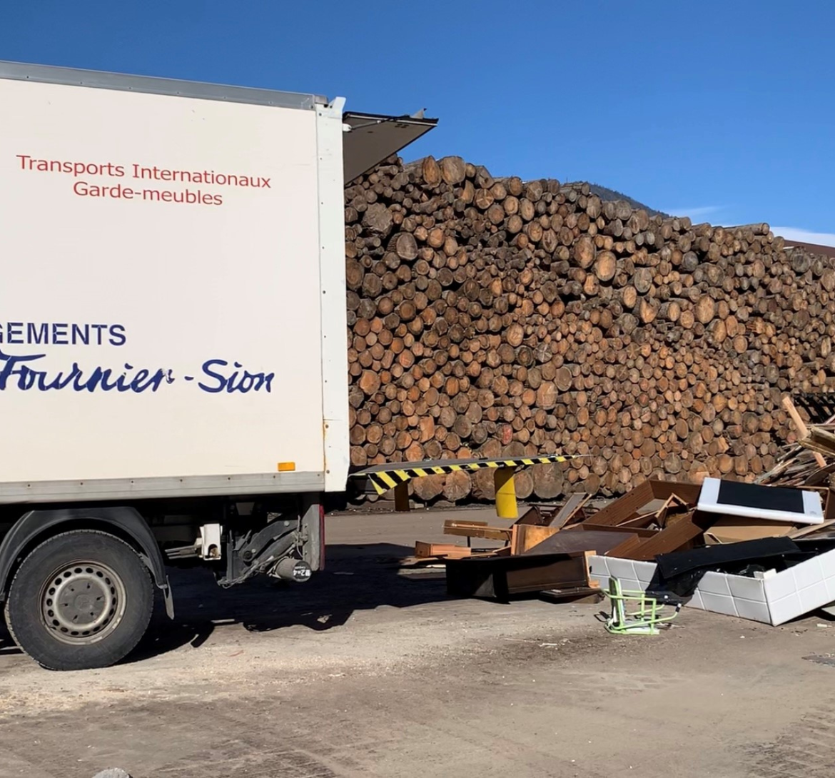 Un camion de l'entreprise Dubuis-Fournier Sion garé devant un tas de débarras et bois