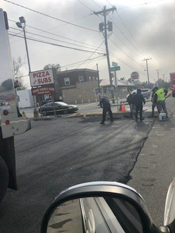 Road work outside a pizza shop. Workers repair asphalt under a cloudy sky.