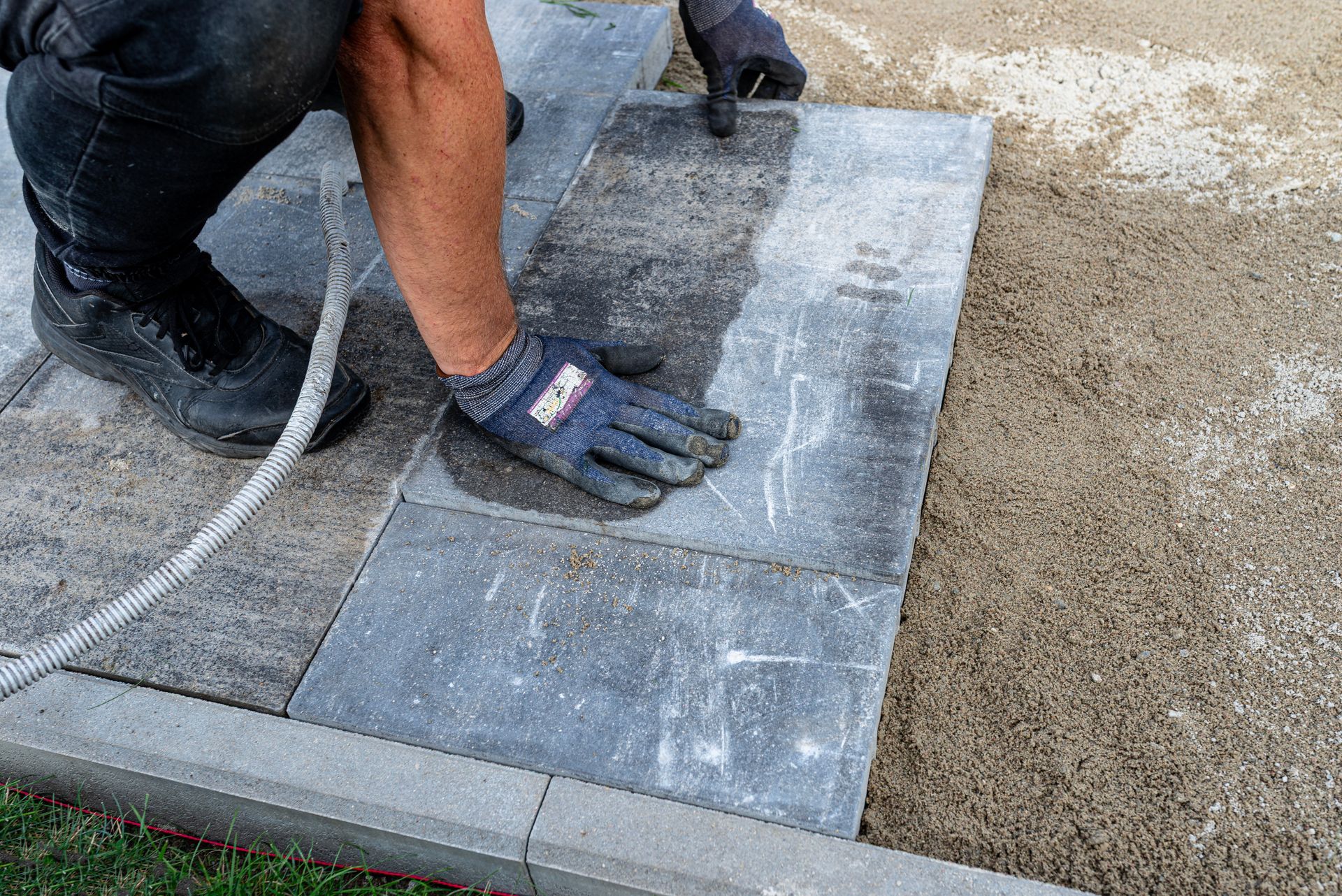 Worker placing a gray stone slab on wet concrete beside a curb