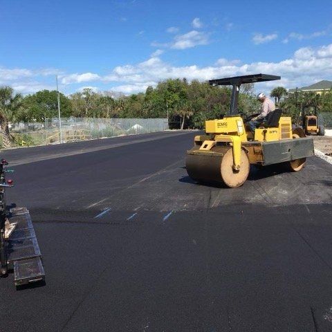 Yellow asphalt roller compacting freshly paved black asphalt; construction site.