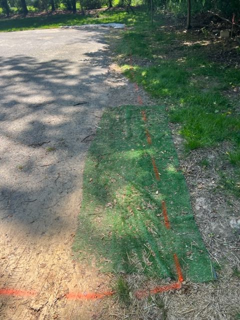 Green netting with orange markings next to asphalt and grass, possibly marking a construction area.