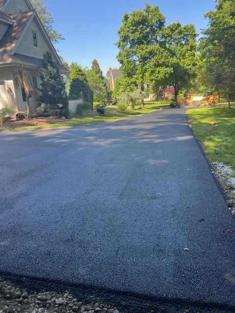 Newly paved asphalt driveway leading toward houses on a sunny day.