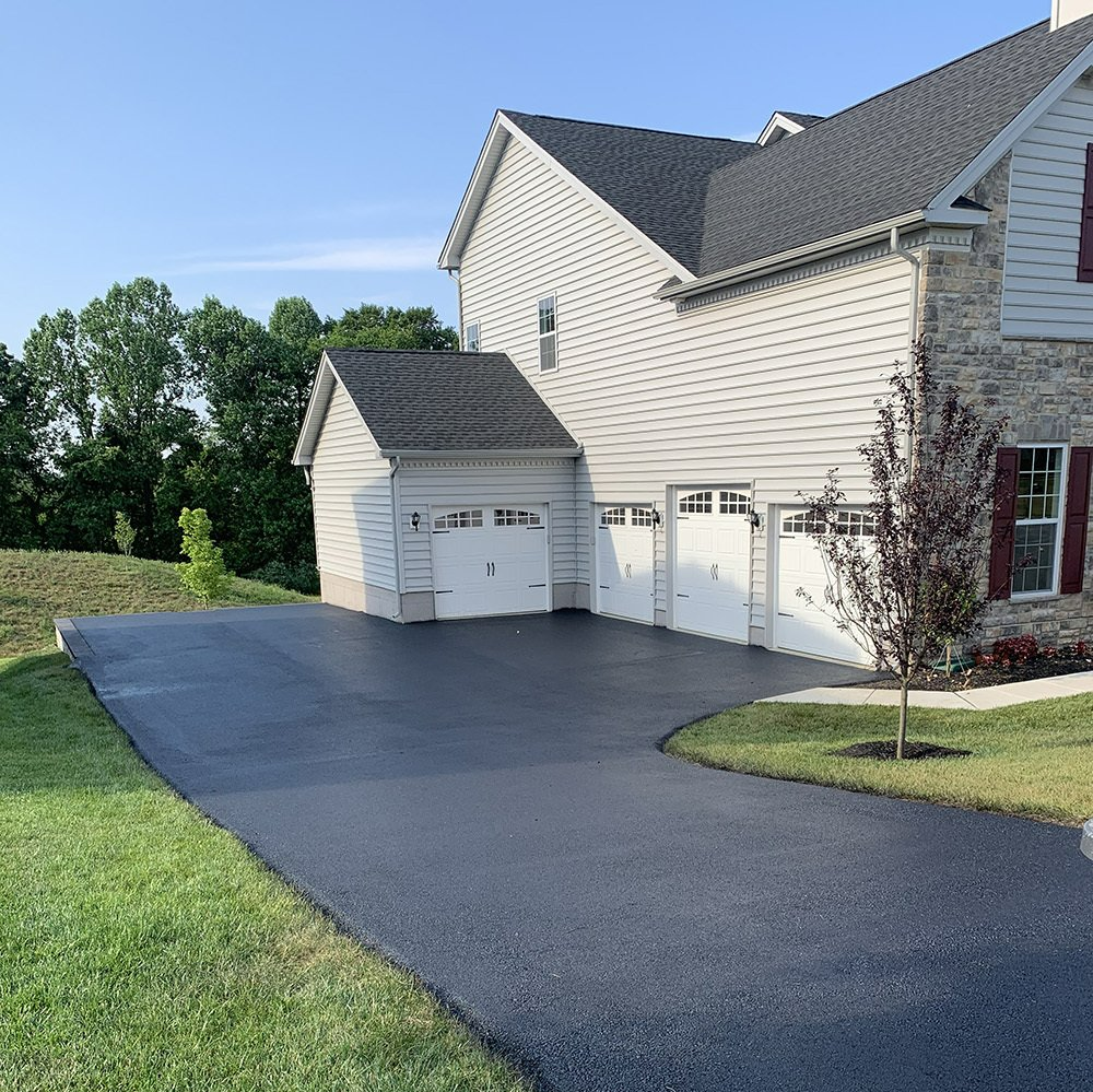 Asphalt driveway leads to a three-car garage attached to a two-story house with gray siding.