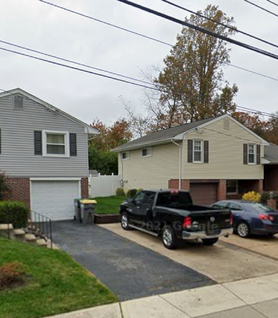 Two-story houses with driveways, a black pickup truck, and a blue car parked outside on a cloudy day.