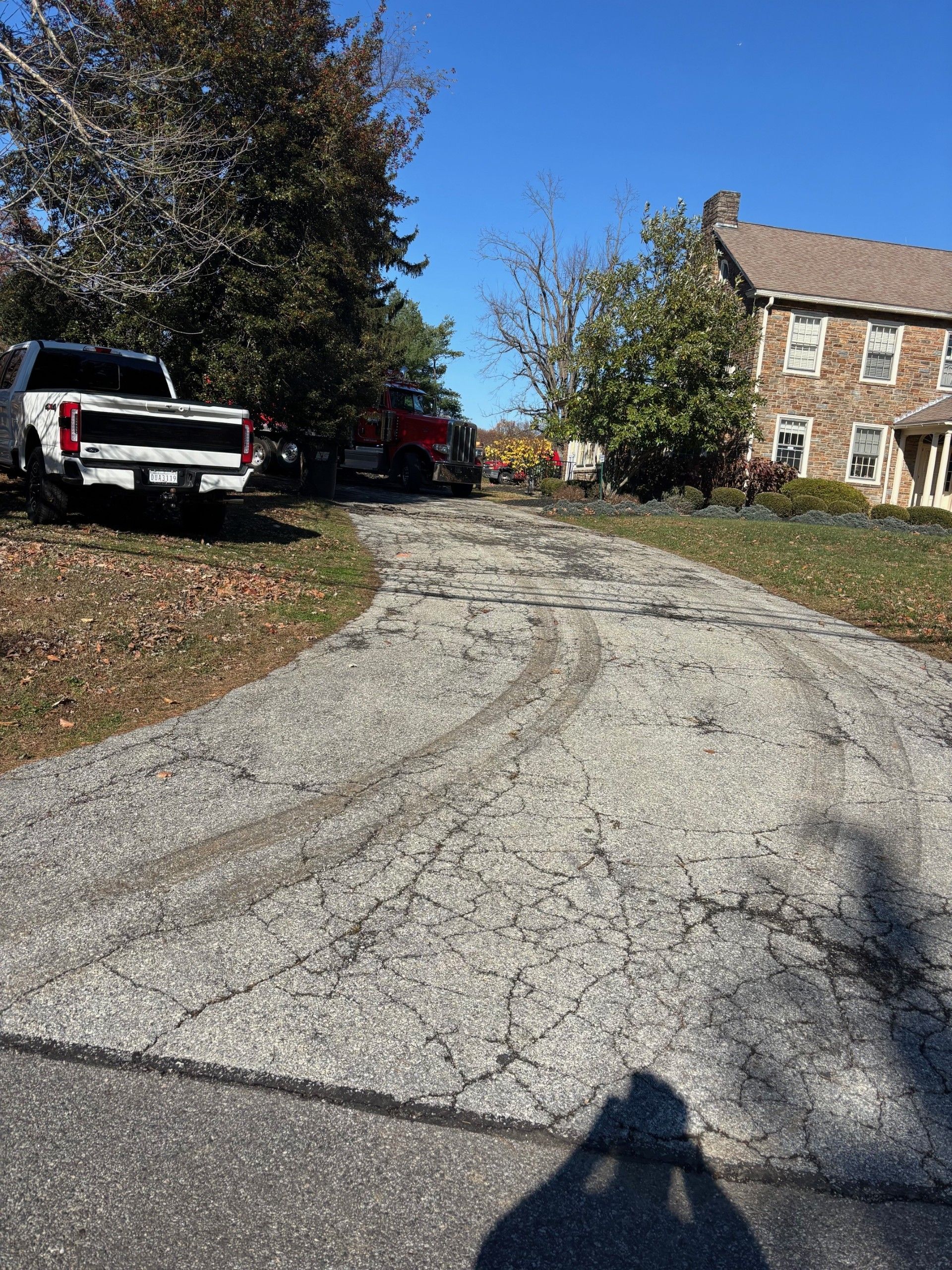 Gravel driveway curving past parked trucks and a stone house on a sunny day