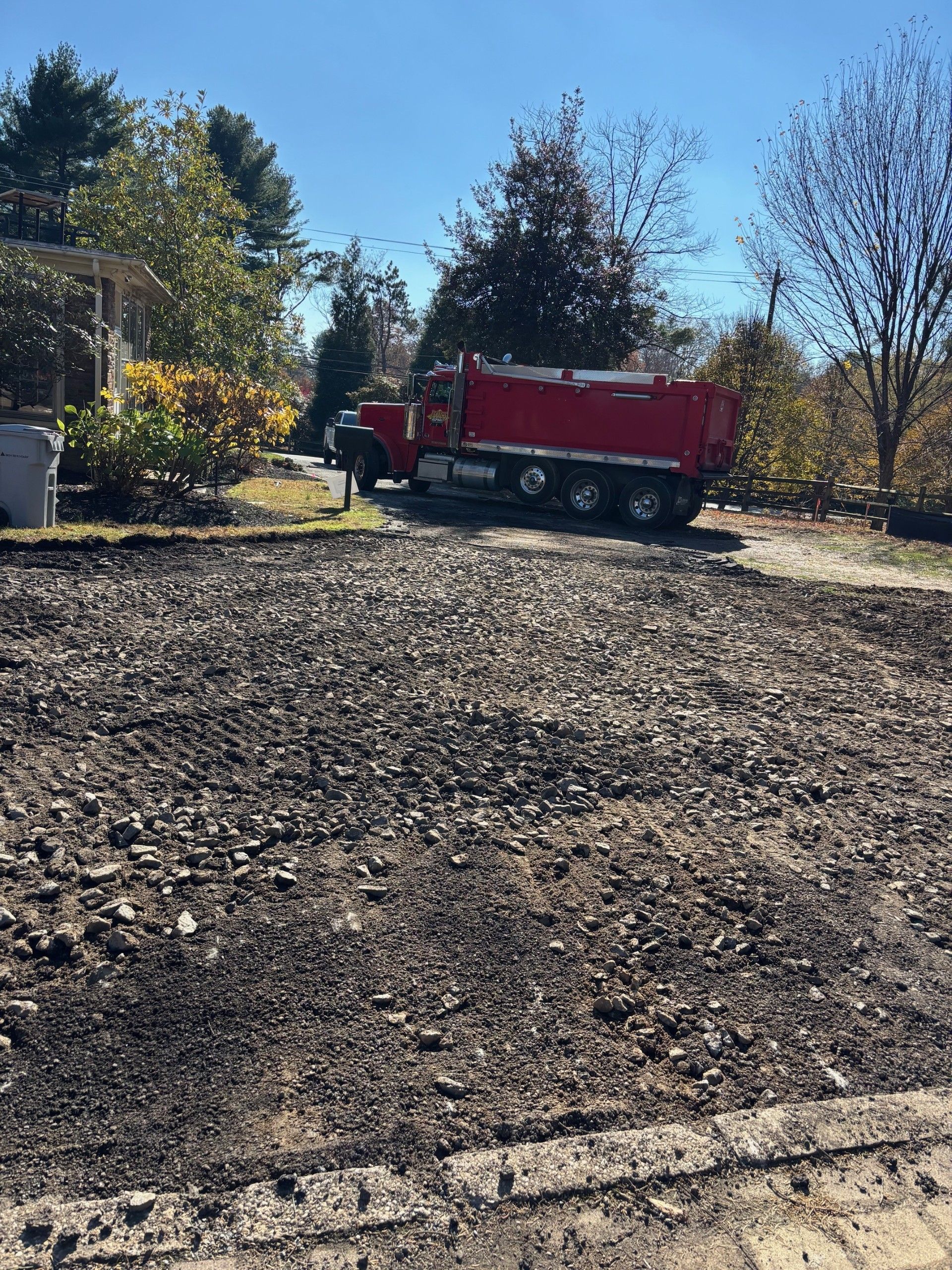Red dump truck parked on a gravel driveway beside trees under a clear blue sky
