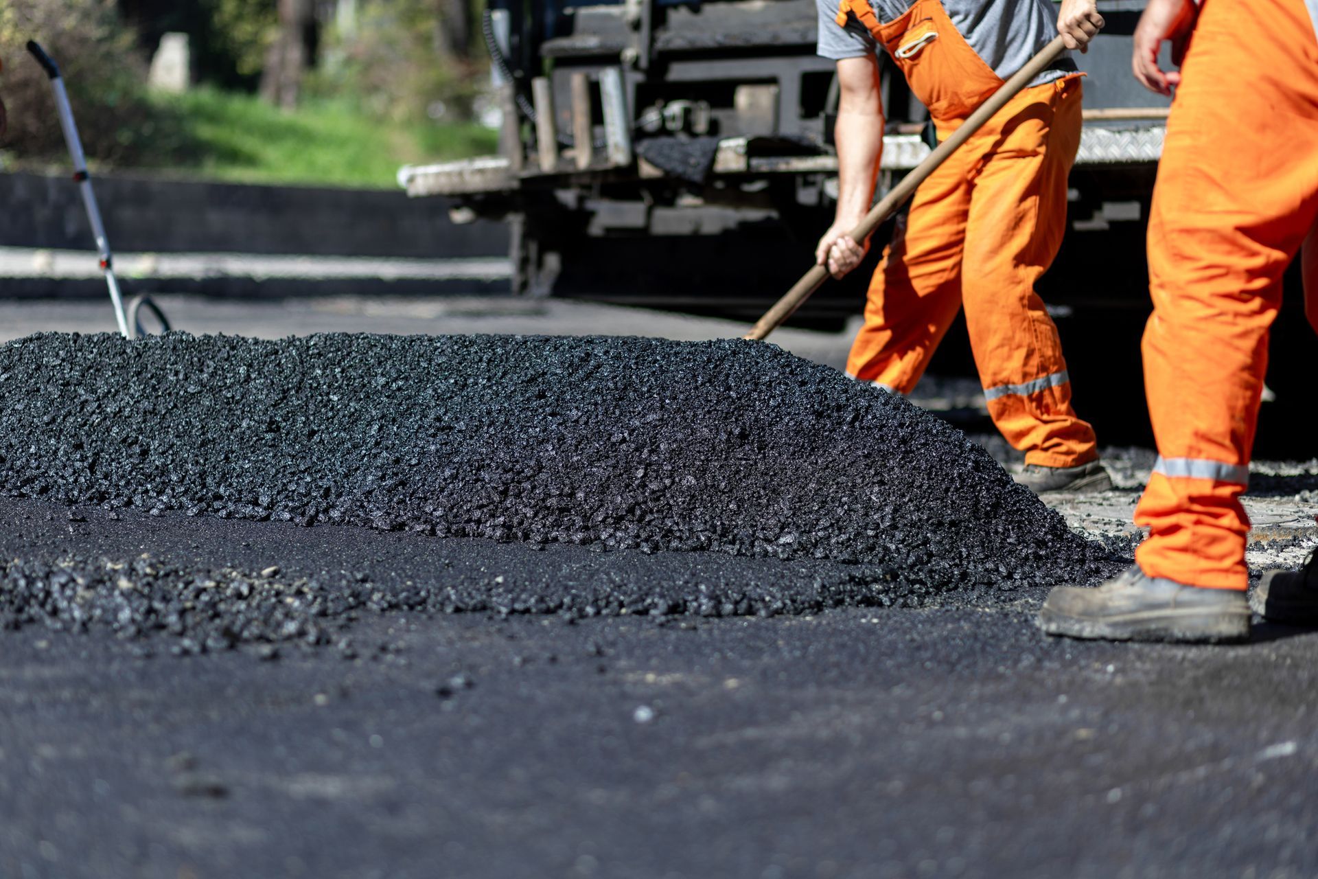 Worker applying asphalt sealant to a roadway with a long-handled squeegee.