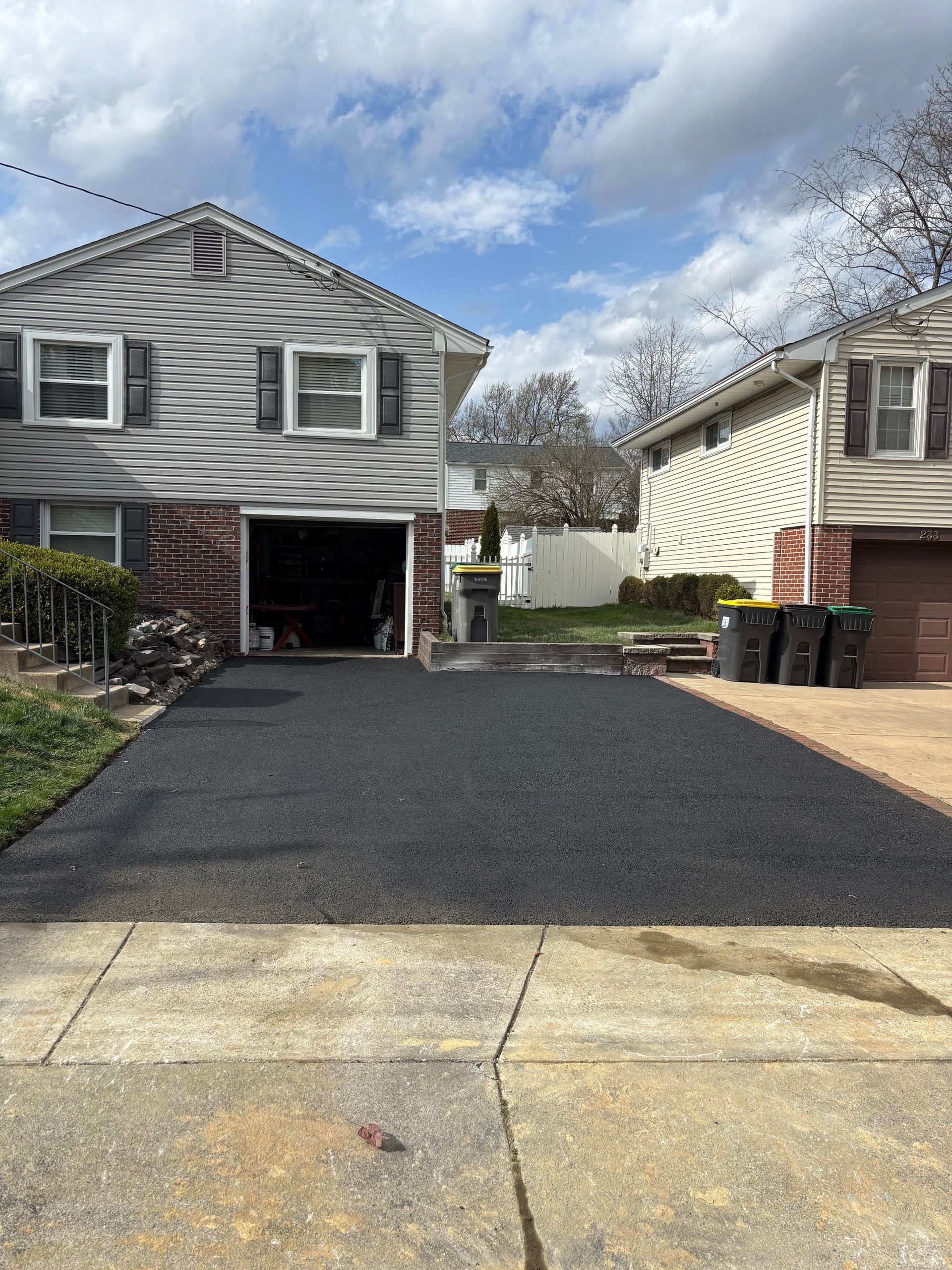 Newly paved asphalt driveway in front of a two-story house with an open garage.