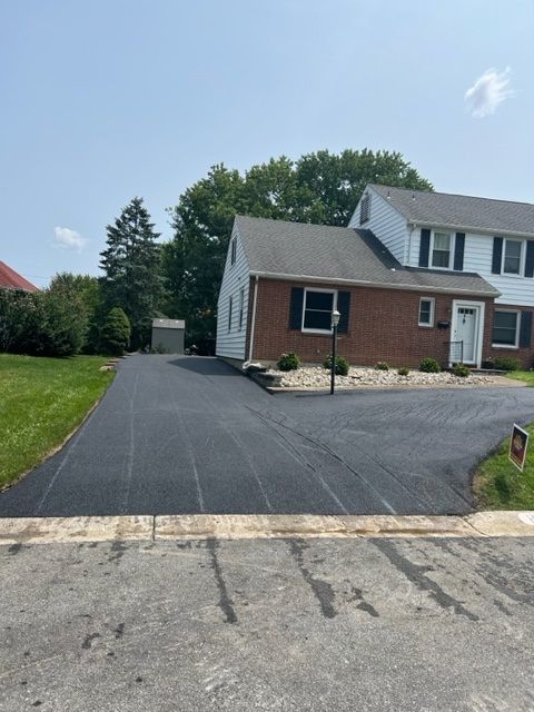 Newly paved asphalt driveway in front of a brick and white siding townhouse on a sunny day.