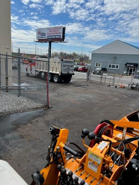 A dump truck is entering a gray lot near a building under a cloudy sky.