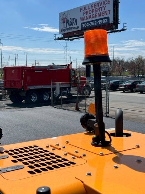 Orange flashing light on construction equipment; red dump truck in background.