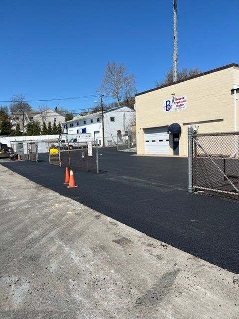 Paved lot with orange cones and building with garage door, blue sky.