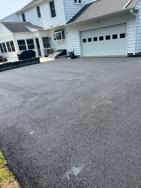 Newly paved asphalt driveway in front of a white house with a garage door.