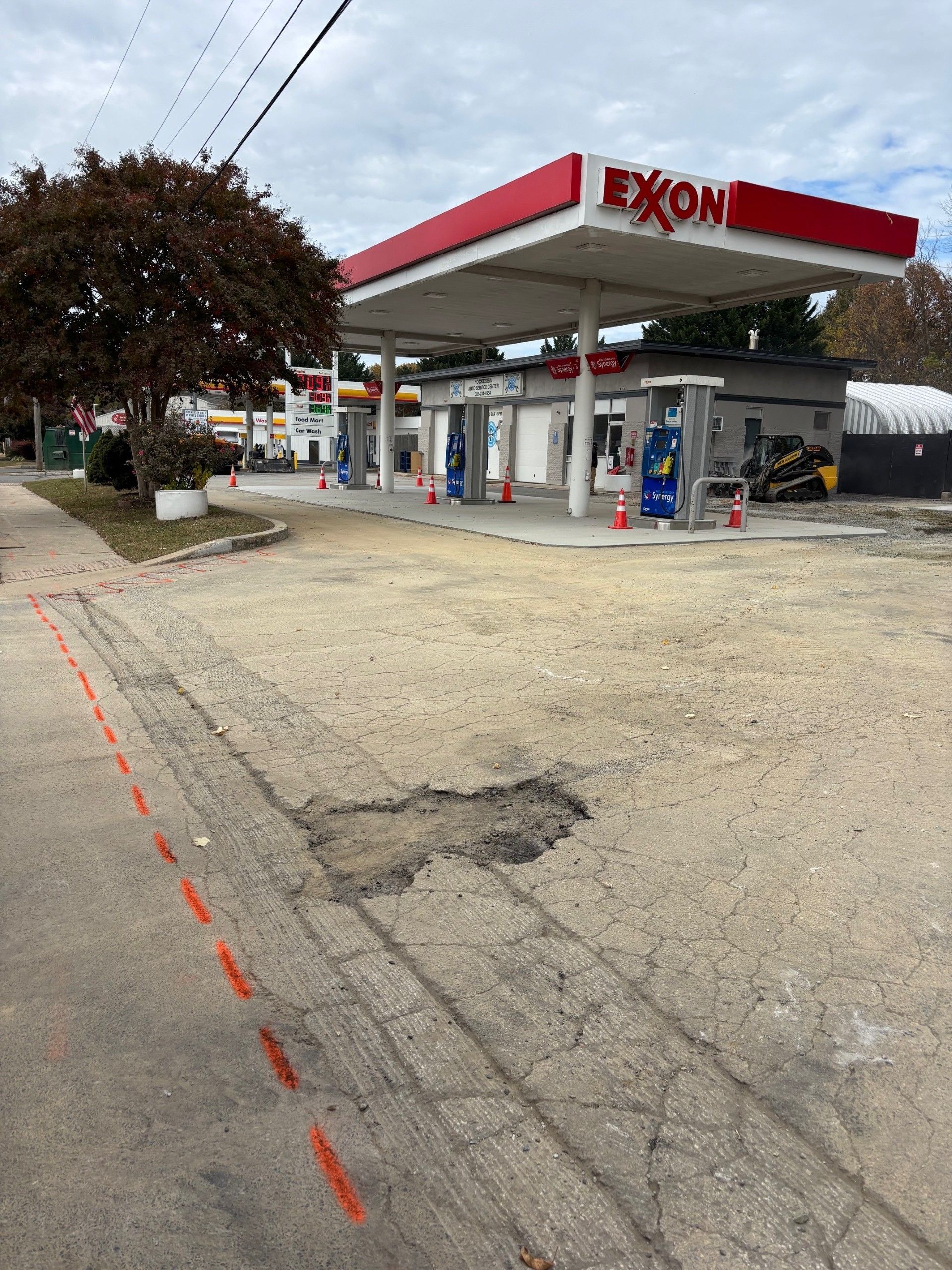 Exxon gas station with red canopy and damaged road surface, including a pothole.