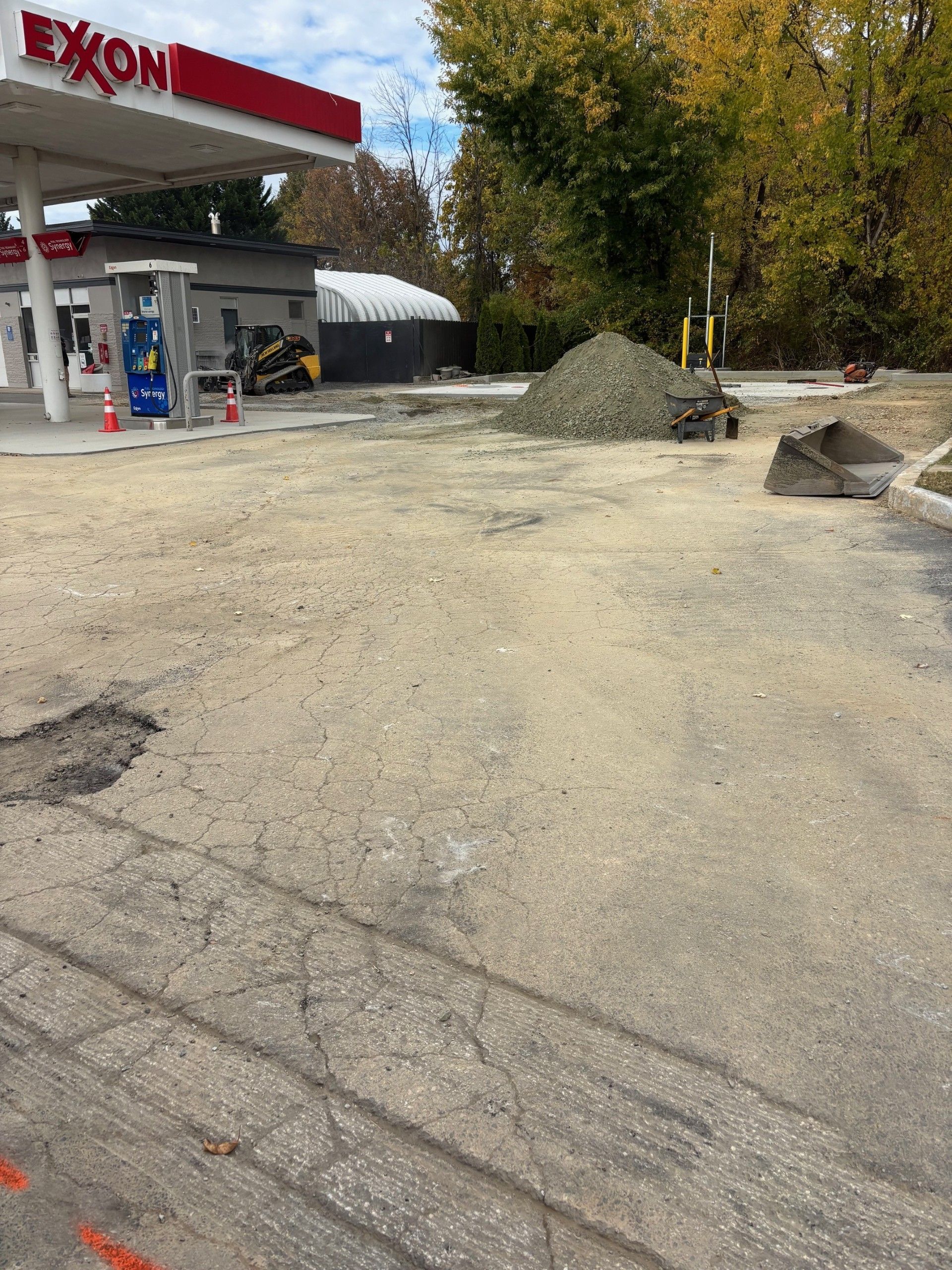 Exxon gas station with construction. Gray pavement, gravel pile, small excavator.