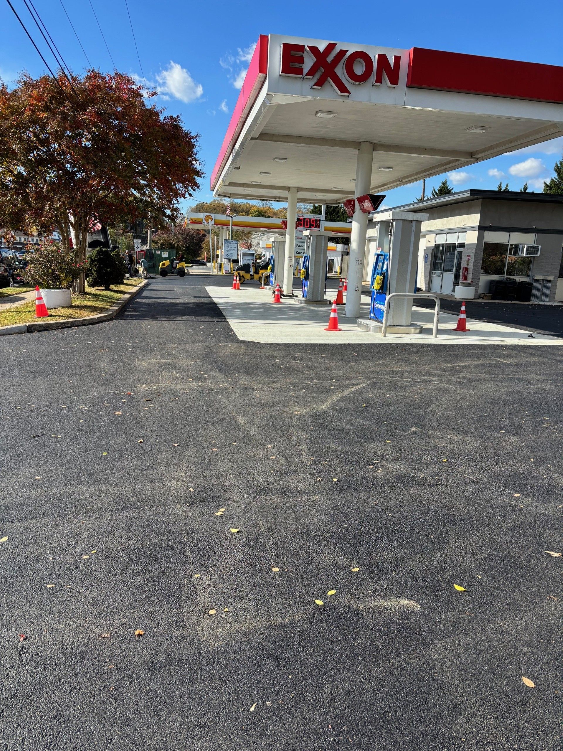 Exxon gas station with red and white canopy, newly paved asphalt, orange cones.