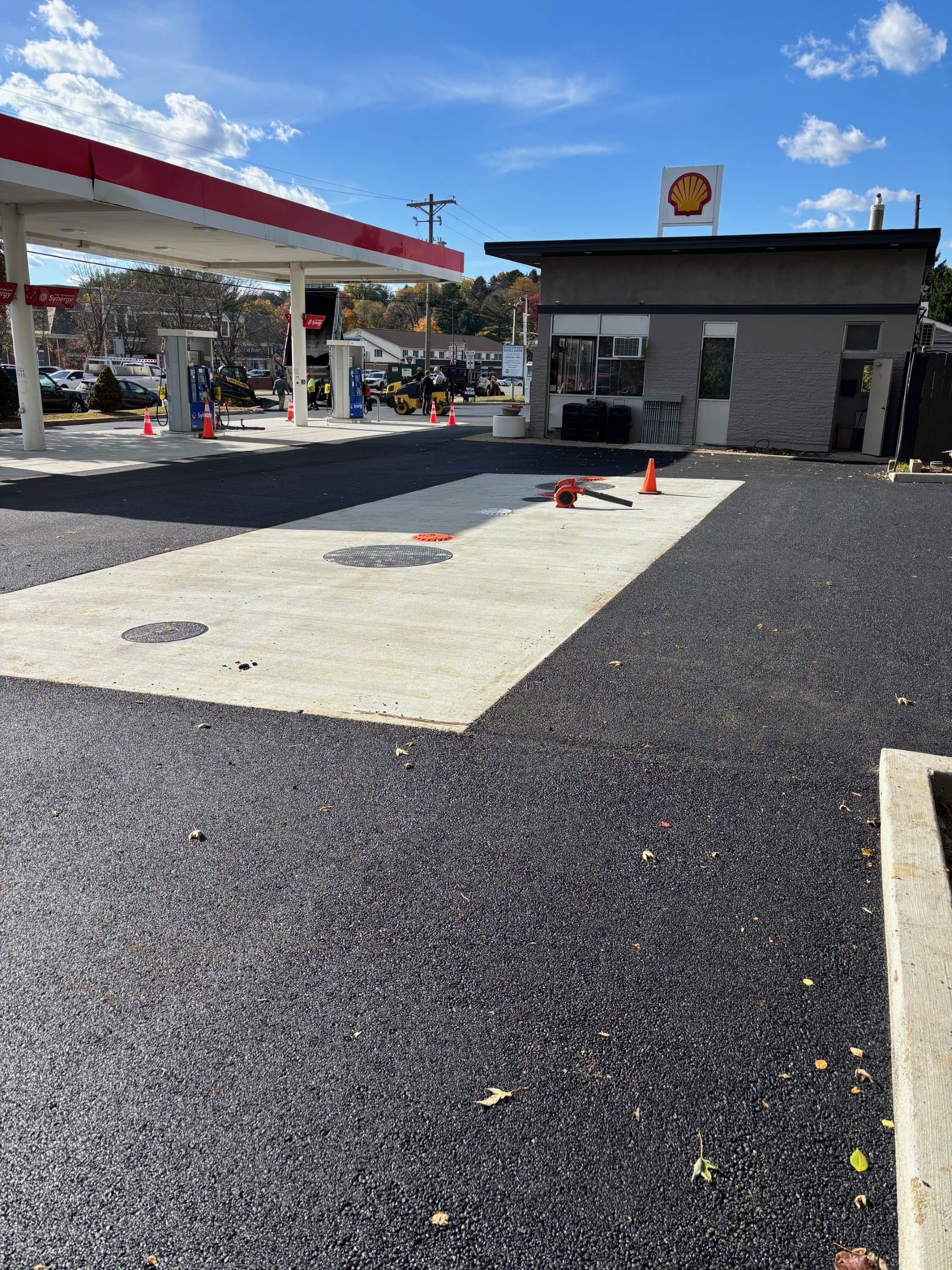 Shell gas station with newly paved asphalt. Canopy with red trim, small building, blue sky.