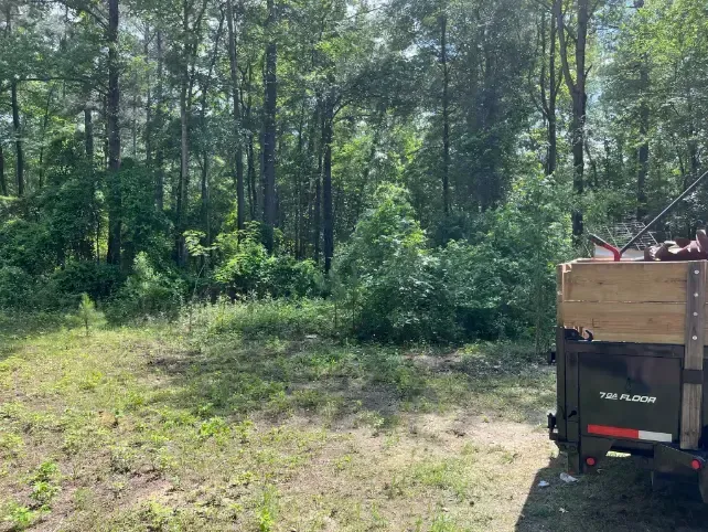 a trailer is parked in a grassy field in the middle of a forest .
