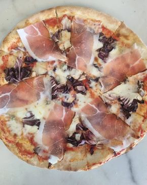 Pizza con prosciutto, radicchio e formaggio su una superficie di marmo.