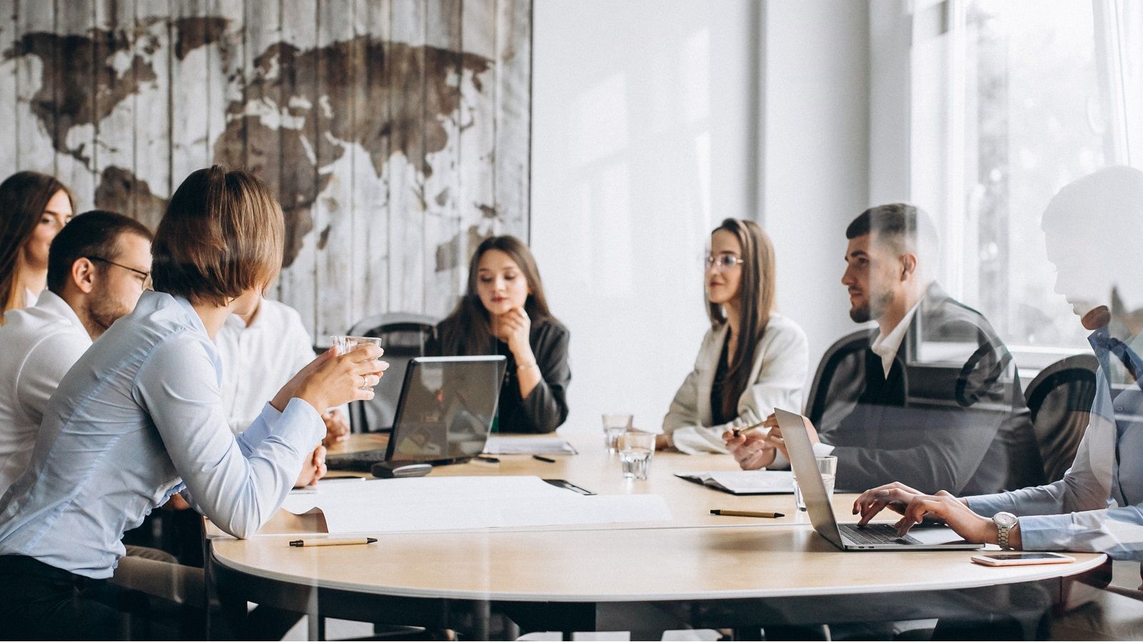 Equipo de diversos profesionales colaborando alrededor de una mesa de conferencias en una oficina moderna con un mapa del mundo en la pared.