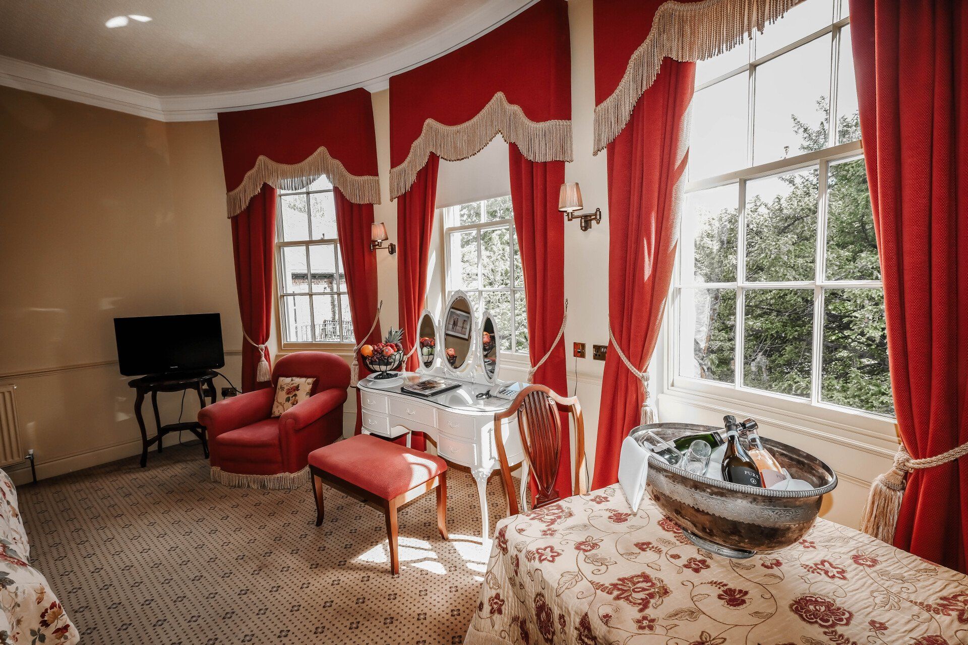 A living room with red curtains , a table , chairs and a television.