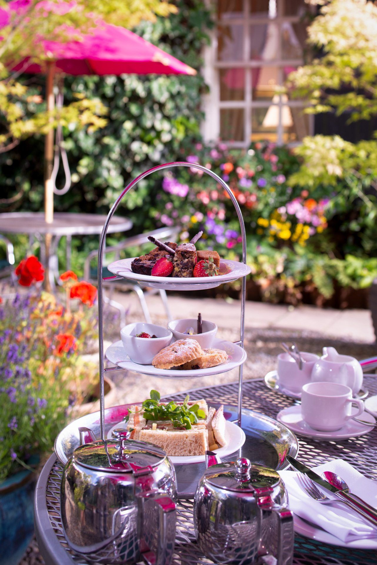 A table with plates of food on it and a pink umbrella in the background.