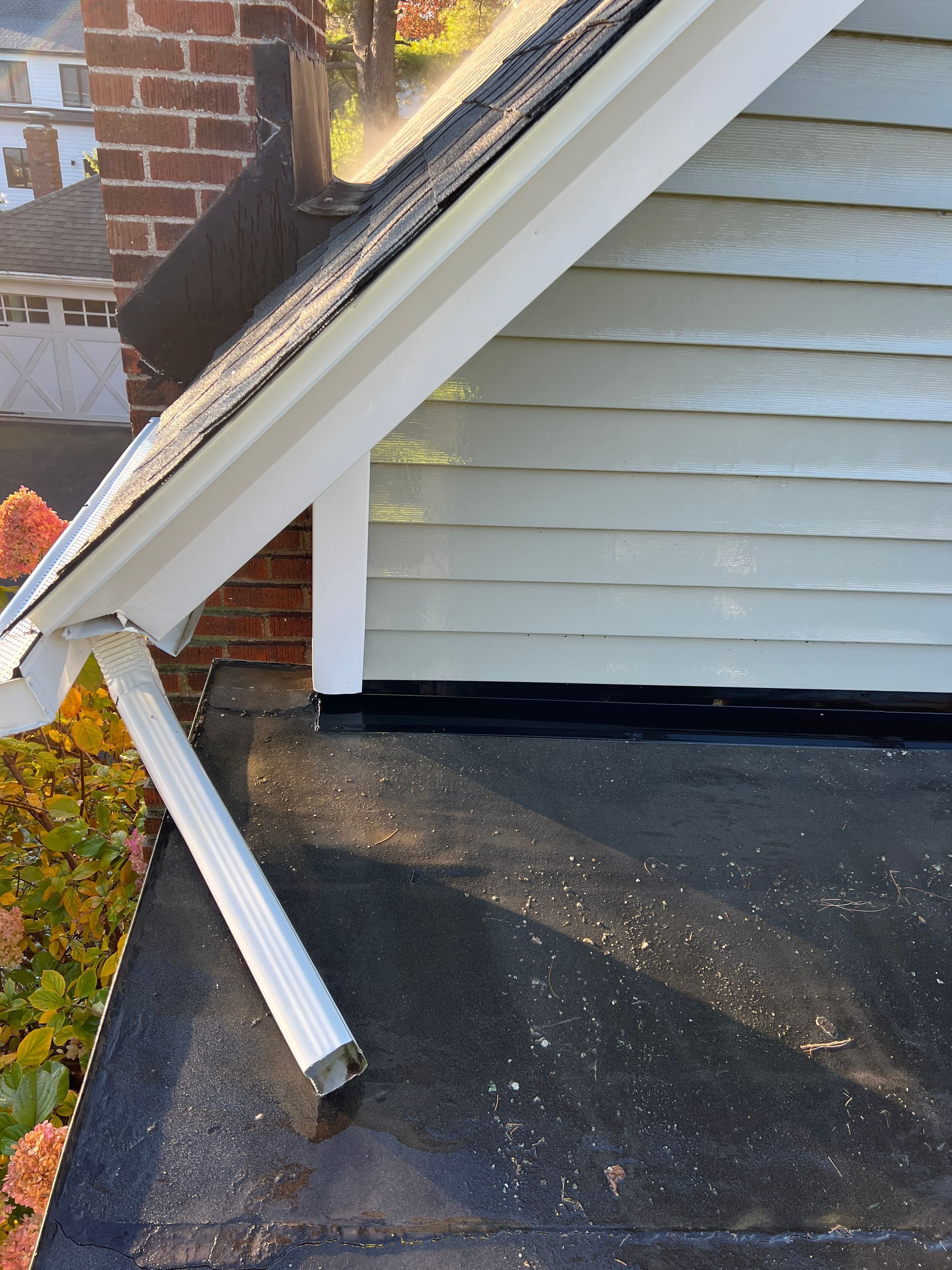 A close-up view of a roof-to-wall transition with black flashing, a white support beam, and light green horizontal siding.