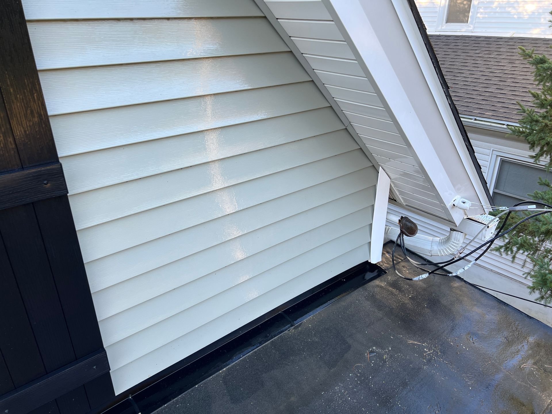 Light-colored vinyl siding meets a black roof flashing and white eaves on the exterior of a house.