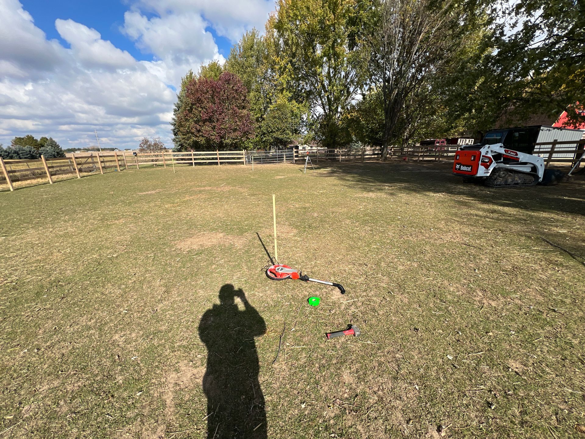 A grassy field with a fence in the background, a small red tool on a stake, and a construction vehicle to the right.