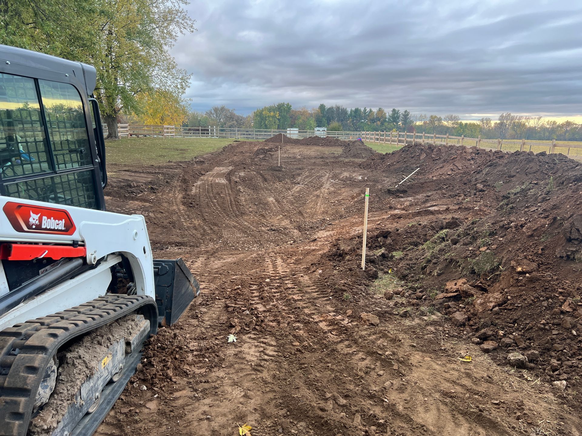 A white Bobcat skid-steer loader sits on a muddy, excavated construction site under a cloudy sky.