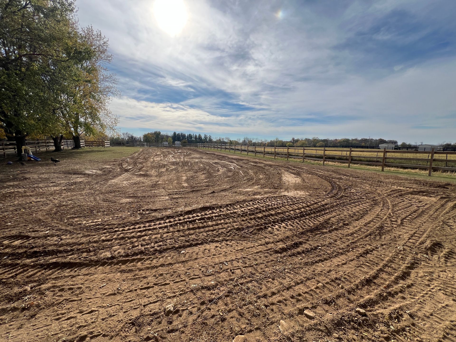 A freshly tilled, dirt field with tractor tire tracks under a bright, sunny sky with scattered clouds.