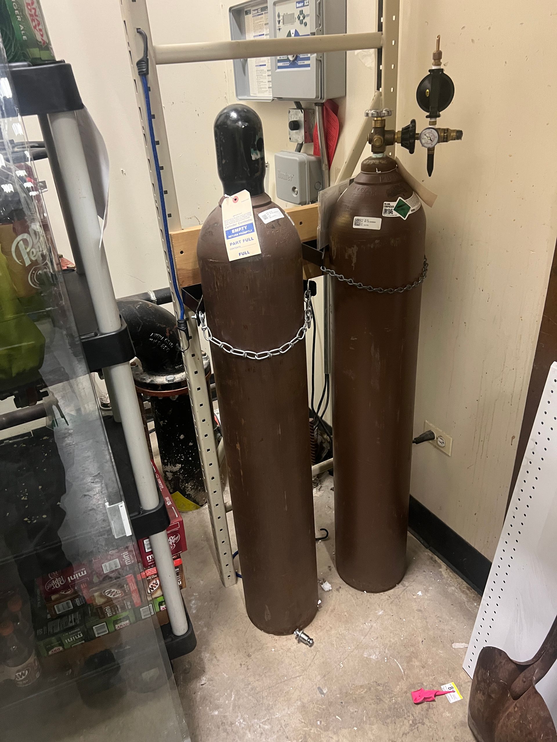 Two brown metal gas cylinders secured by chains to a rack inside a storage area.