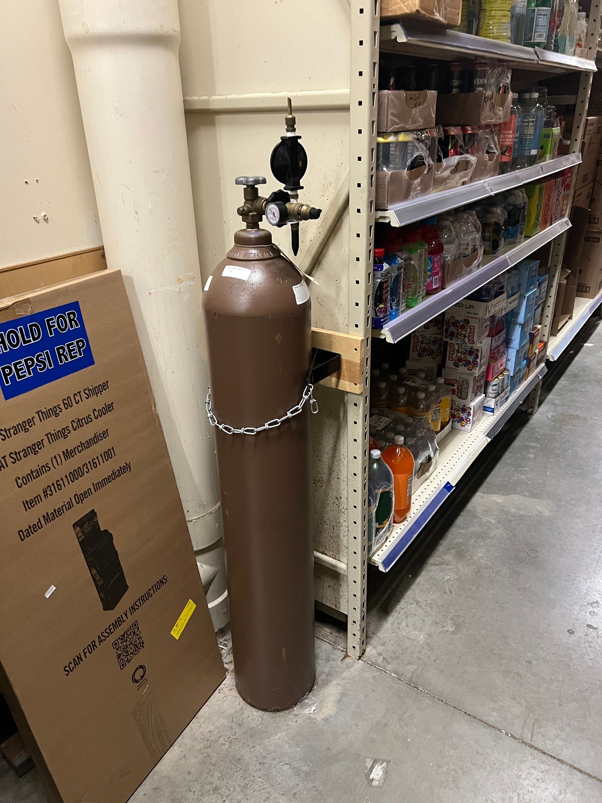 A brown compressed gas cylinder chained to a metal retail shelf in a store aisle.