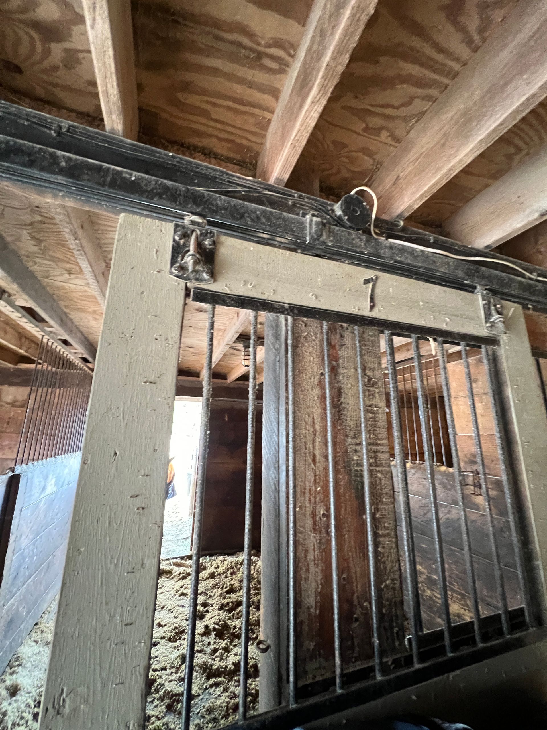 A view from inside a horse stall, showing the top of a sliding metal door marked with the number seven.