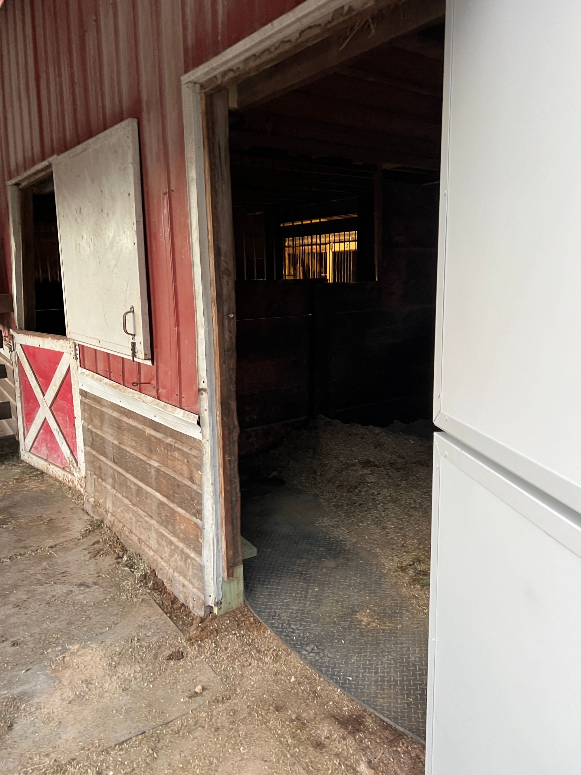 A view into a rustic barn's open doorway, showing hay on the floor and a glimpse of a light inside.