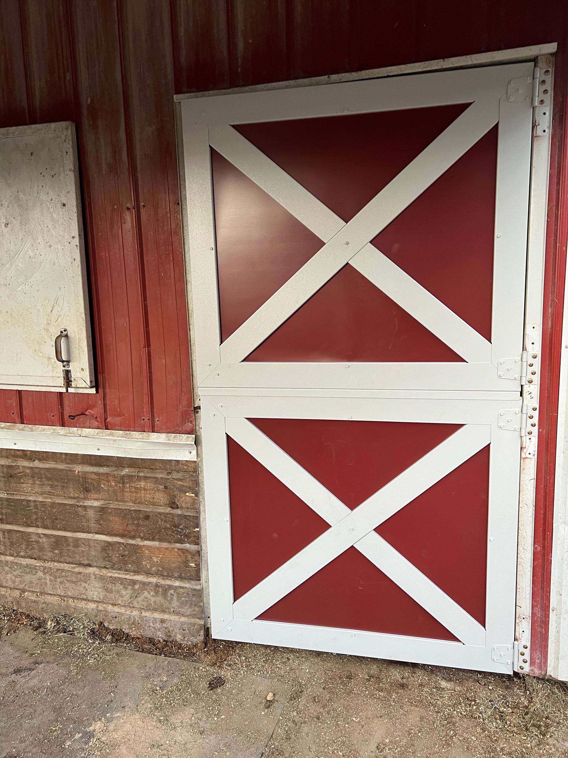 A red and white Dutch-style barn door with an X-pattern next to a brick wall and a small window.