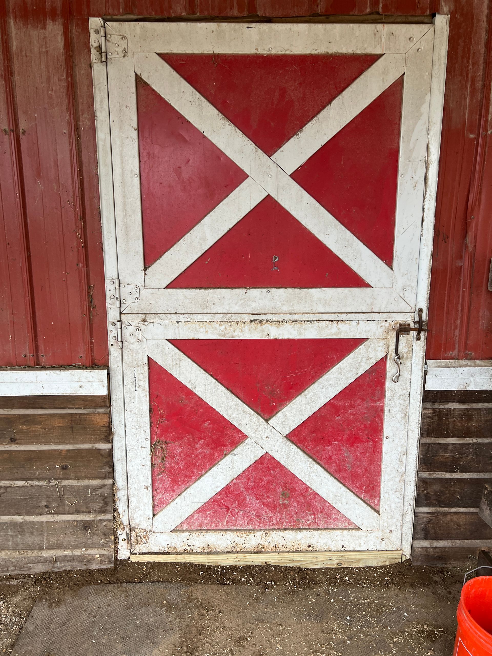 A rectangular barn door with red panels and white cross-bracing, set into a wooden red and brown wall.