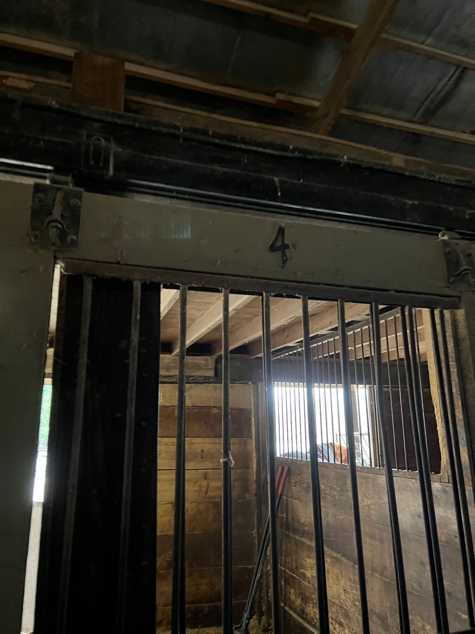 A metal-barred horse stall gate with the number 4 painted above the doorway inside a rustic wooden barn.