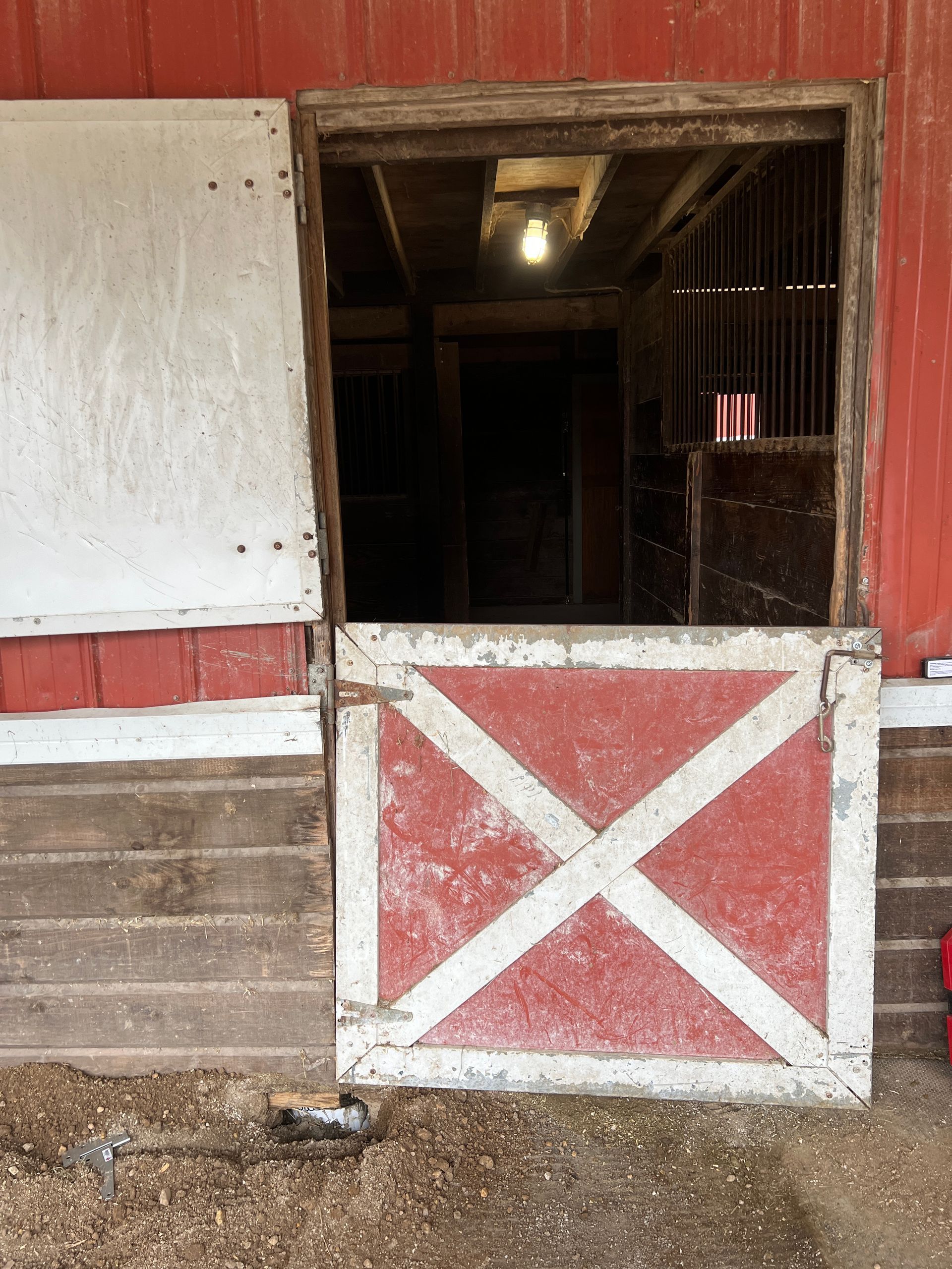 A red and white barn door is open to a dim interior with a light fixture on the ceiling.