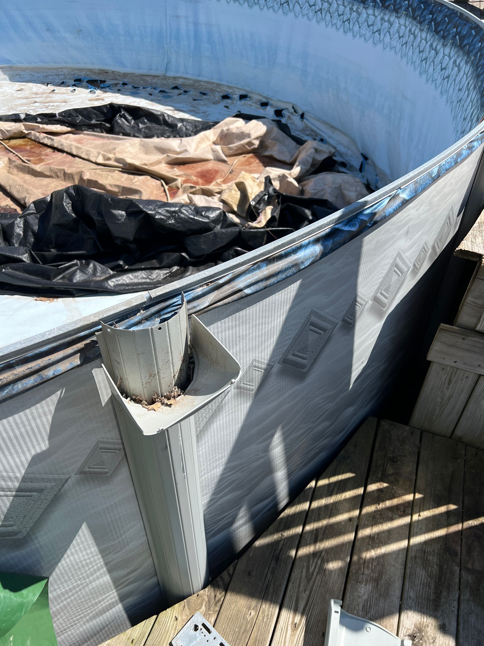 An above-ground pool under repair, showing an exposed frame and support post with a pool cover resting inside the liner.