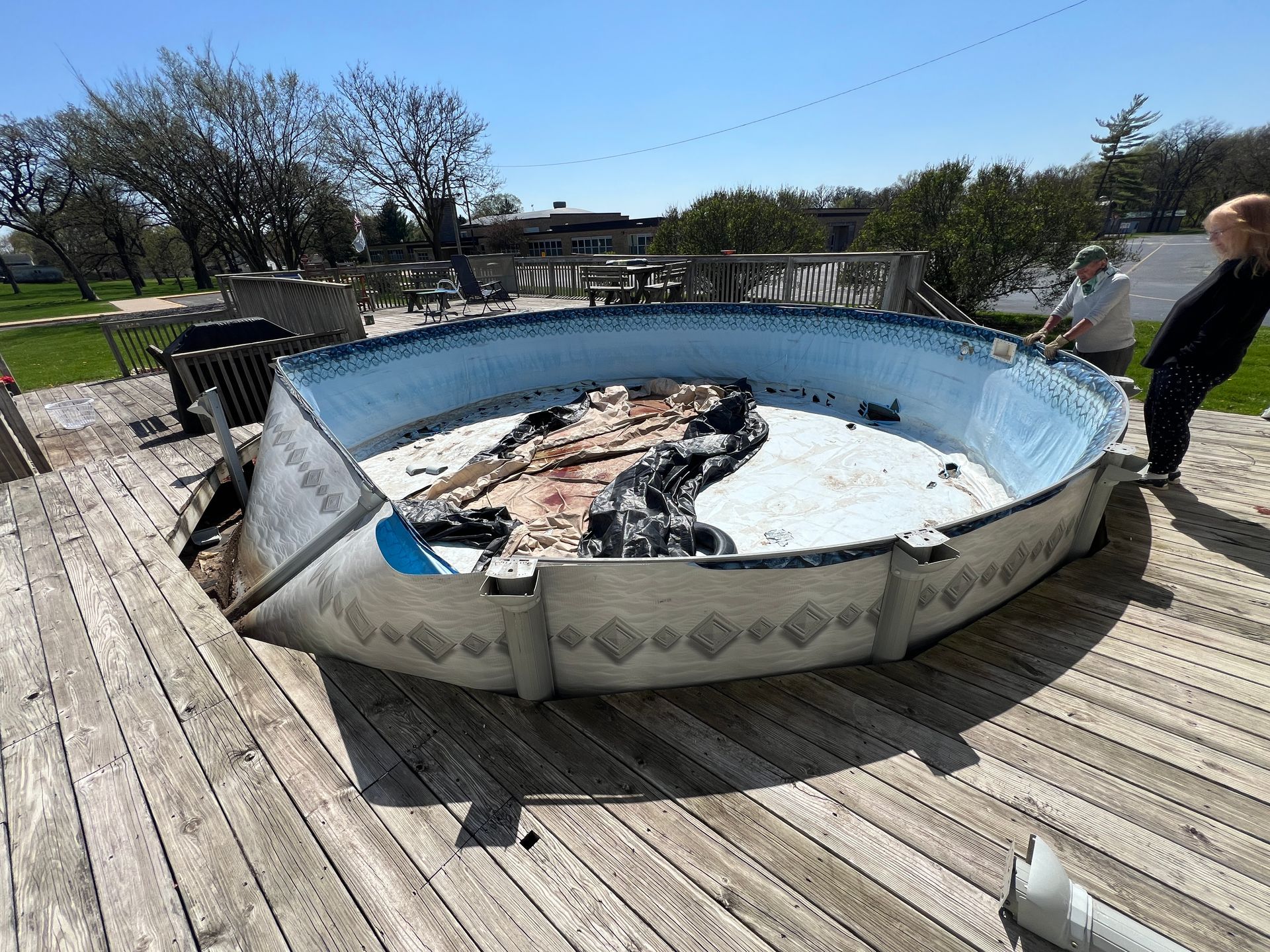 An above-ground pool sits on a wooden deck, its side collapsed inward with damaged liner visible inside.
