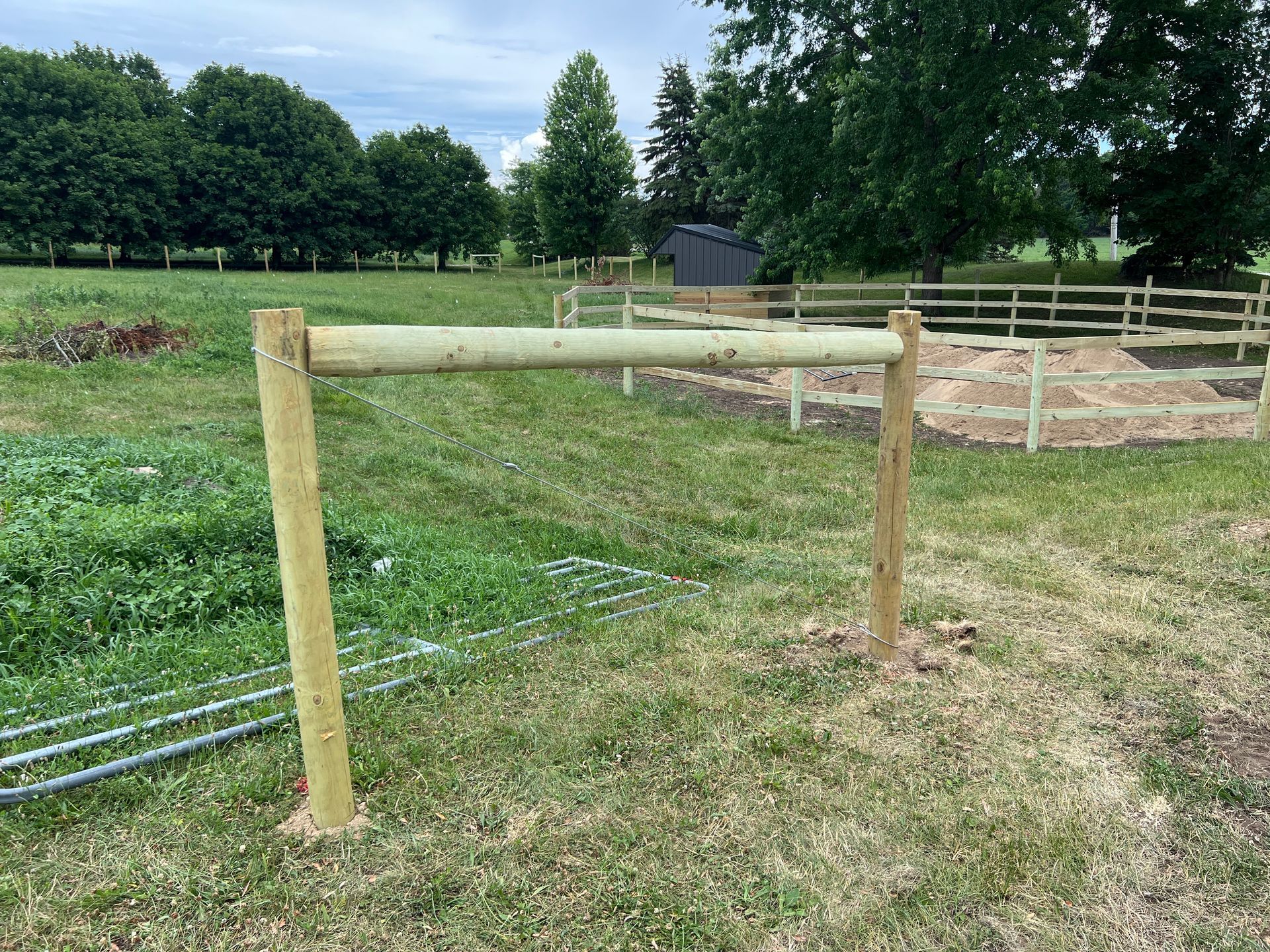 Two wooden posts connected by a horizontal rail stand in a grassy field with a fenced garden in the background.