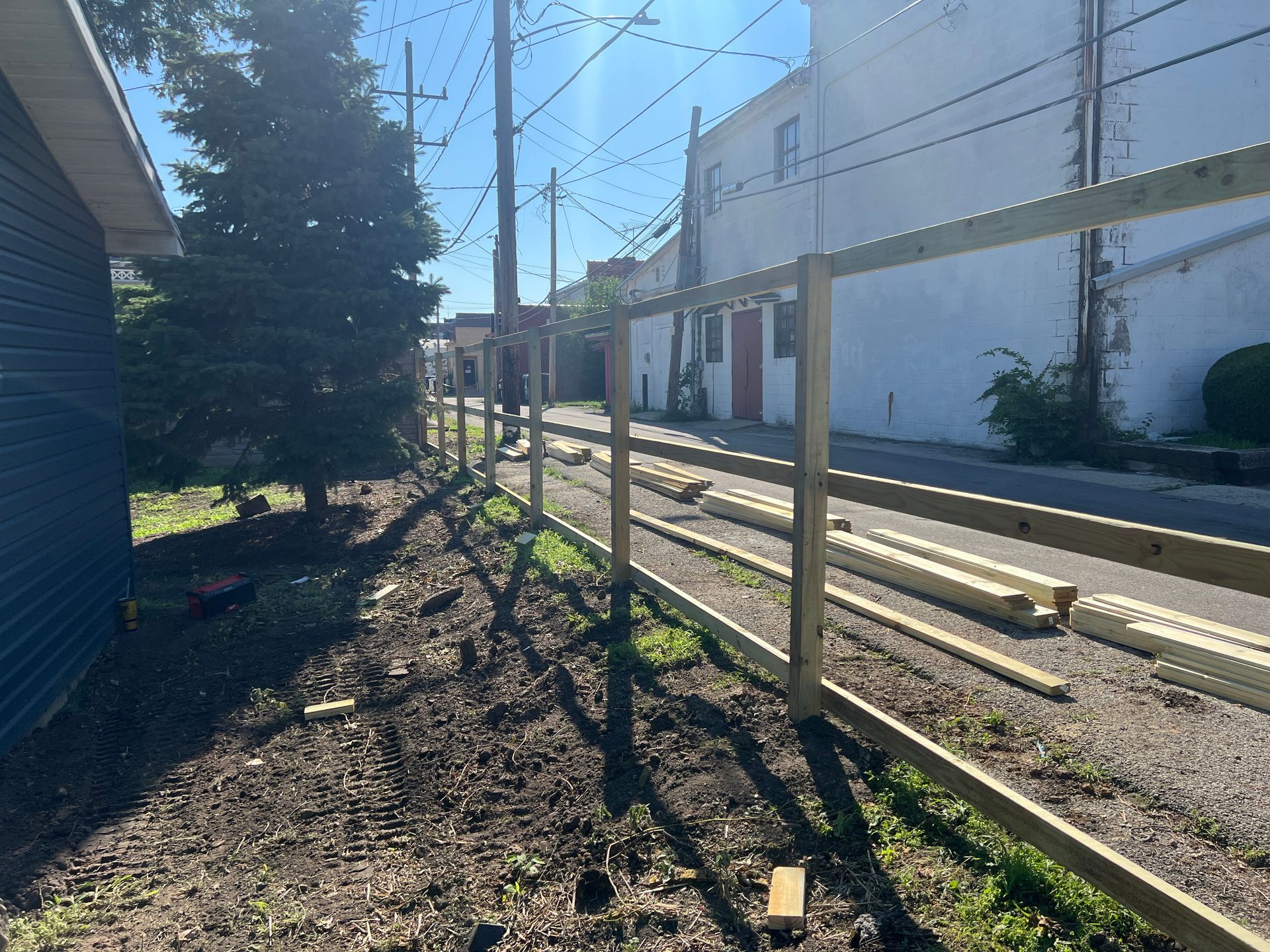 A wooden fence frame under construction along a dirt path next to a building.