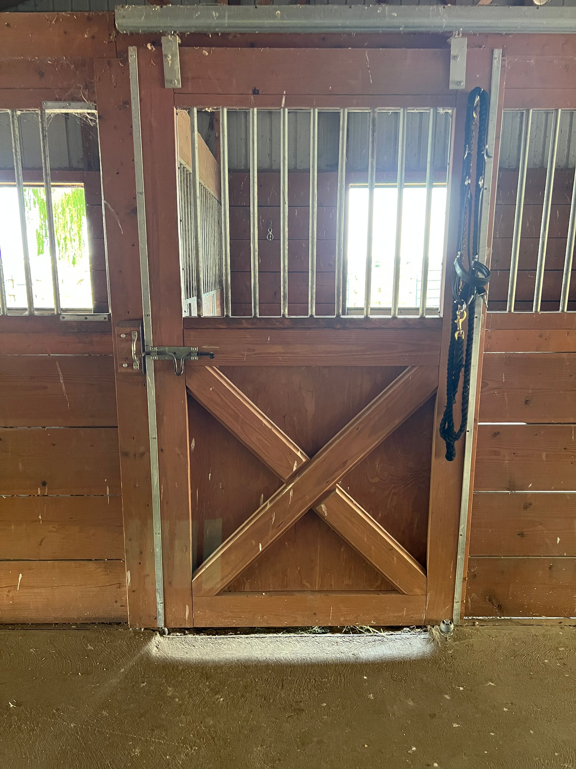 A wooden horse stall door with metal bars, a latch, and a black halter hanging on the right side.