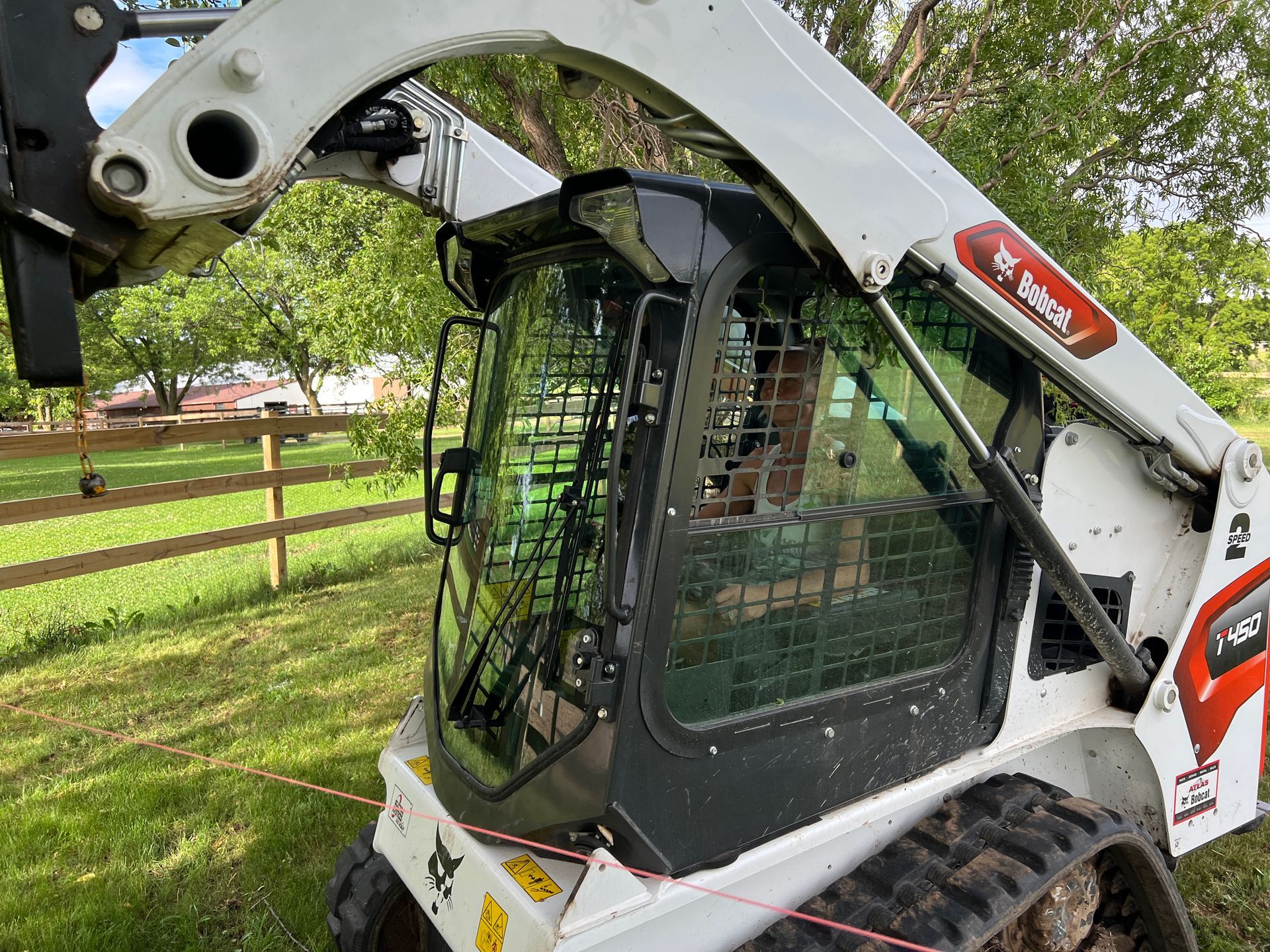 A white Bobcat compact track loader sits on a grassy field in front of a wooden fence.